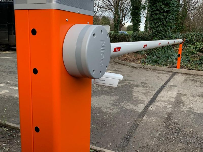 Close-up of an orange Nice barrier cabinet with a Hikvision reader mounted on the side and the boom extended