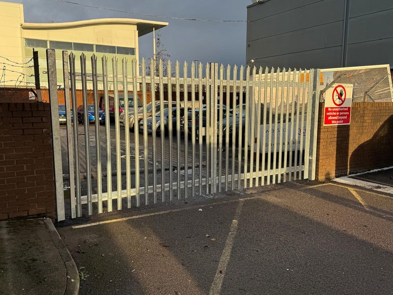 Galvanised palisade gate closing off a commercial car park, with a no unauthorised access sign on the pillar