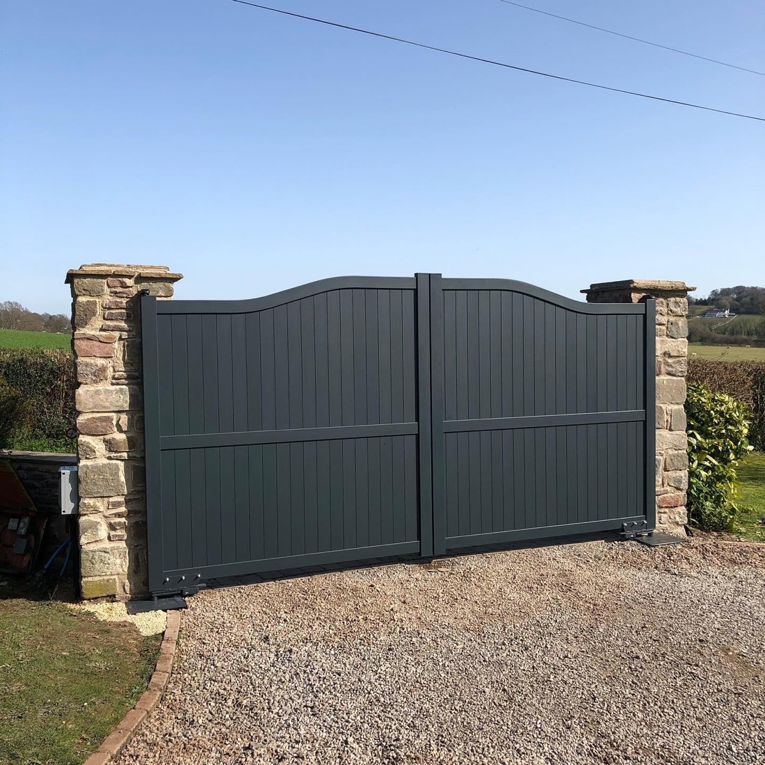 MonGate Essential aluminium electric swing gates with a swept top, installed between stone pillars